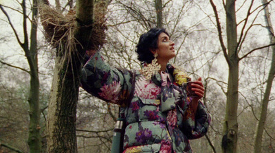 a woman standing in the woods with a bird nest in her hand