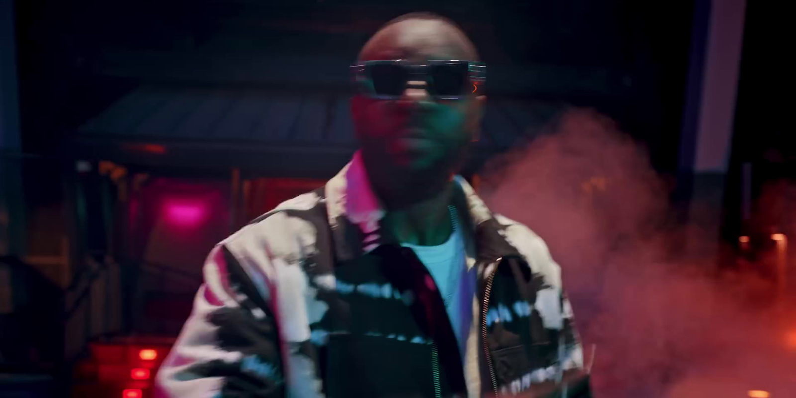 a man wearing sunglasses and a tie standing in a dark room