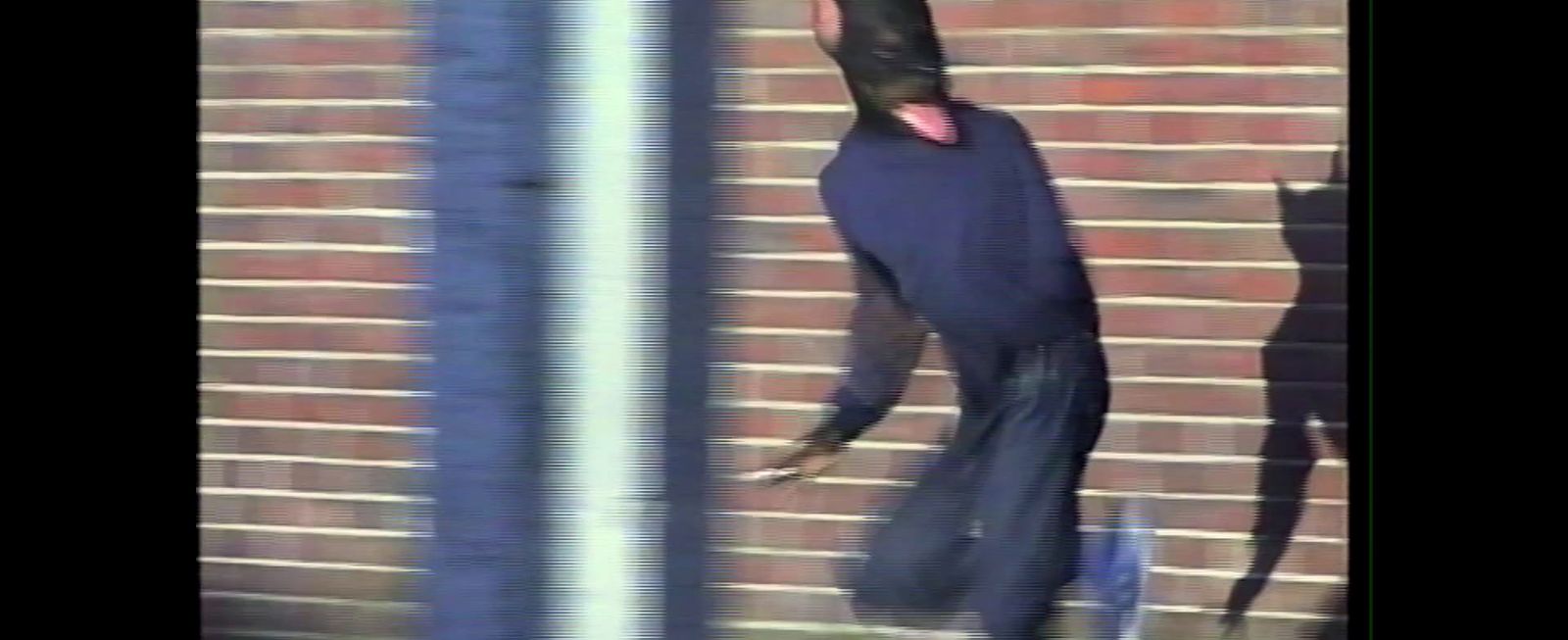 a man in a black outfit standing next to a brick wall