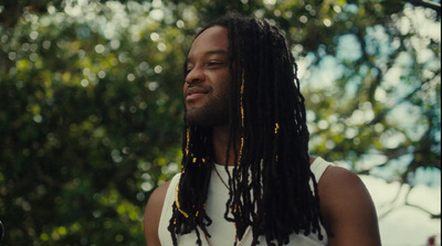 a man with dreadlocks standing in front of trees