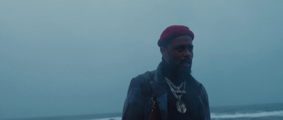 a man with a beard and a red hat standing in front of the ocean