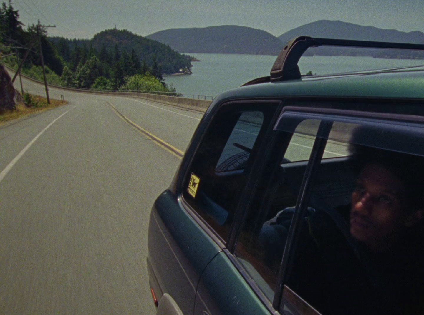 a man driving a car down a road next to a body of water