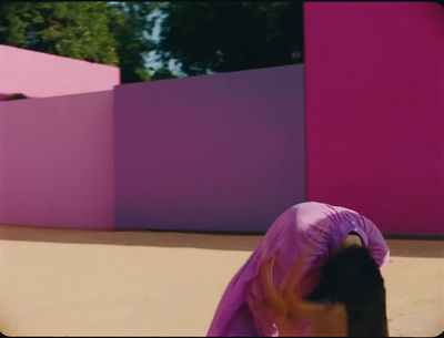 a woman in a purple dress standing in front of a pink wall