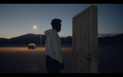 a man standing next to a door in the middle of a desert