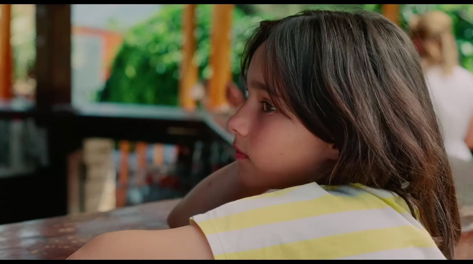 a young girl sitting at a table with her head turned to the side