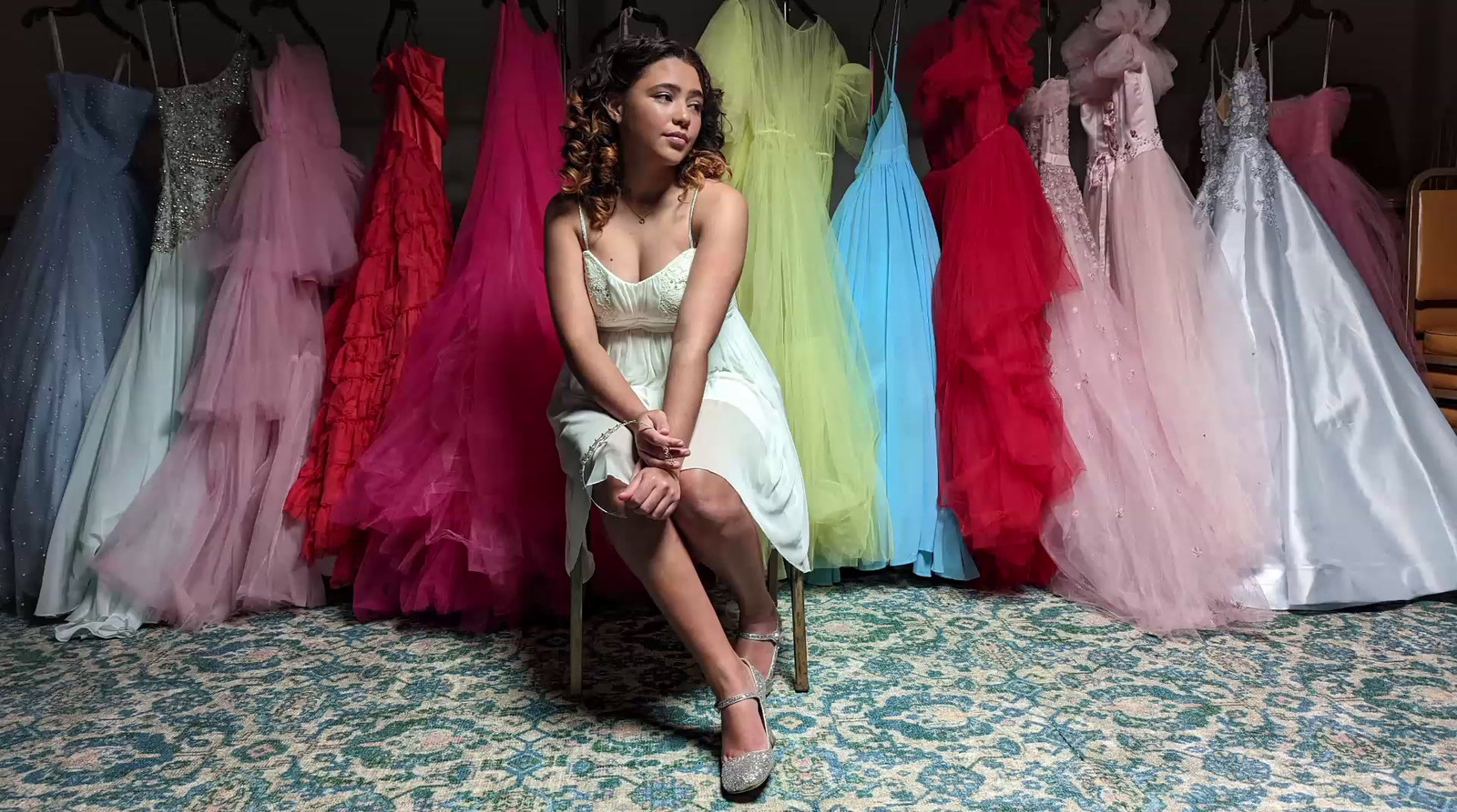 a woman sitting on a chair in front of a rack of dresses