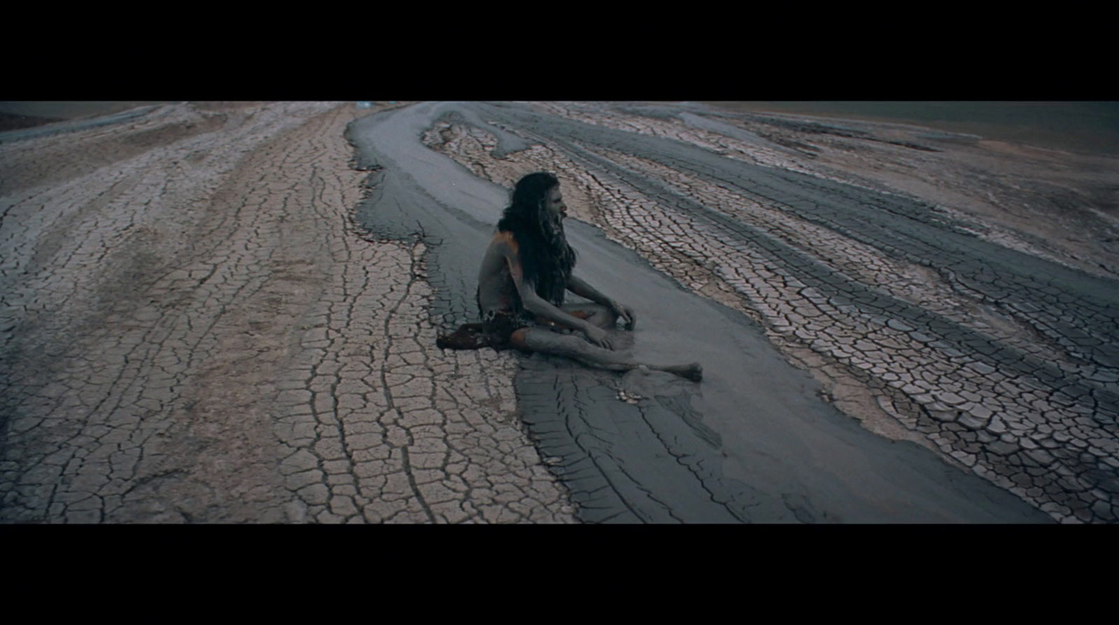 a woman sitting on the ground in the middle of a desert