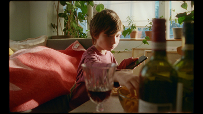 a little girl sitting at a table with a bottle of wine and a cell phone