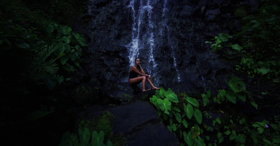 a woman sitting on a rock in front of a waterfall