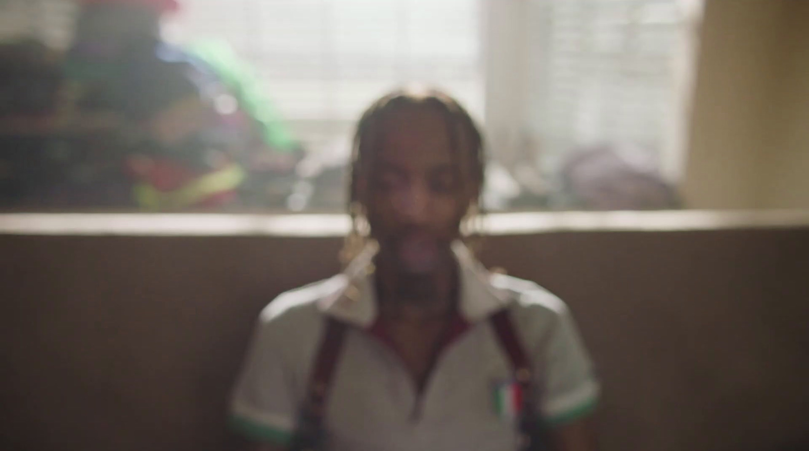 a man with long hair and suspenders standing in front of a window