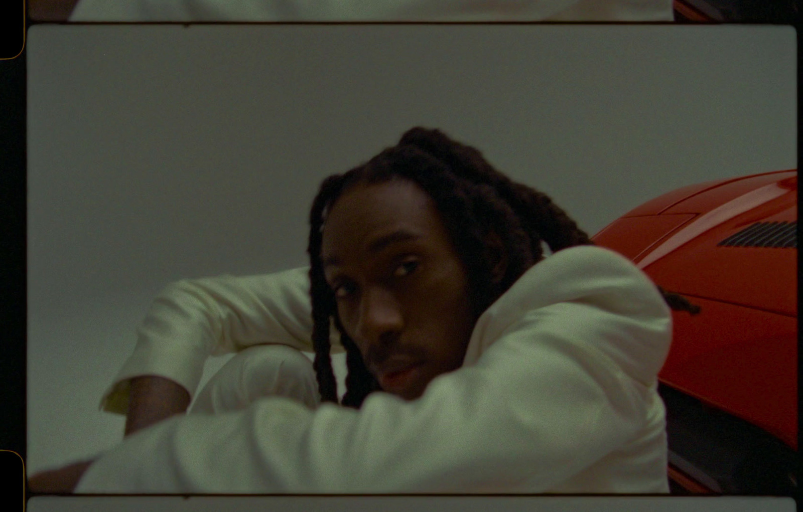 a man with dreadlocks sitting in front of a red car