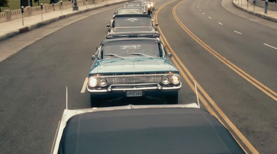 a row of old cars driving down a street