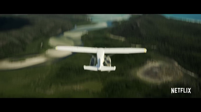 a small white airplane flying over a lush green forest