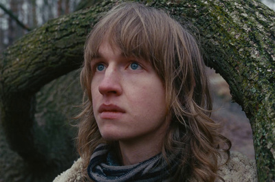 a man with long hair standing in front of a tree