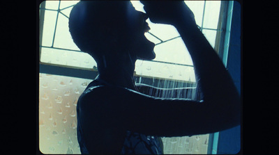 a man standing in front of a window drinking from a bottle