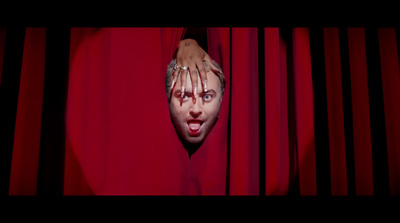 a man with his hands on his face peeking out from behind a red curtain