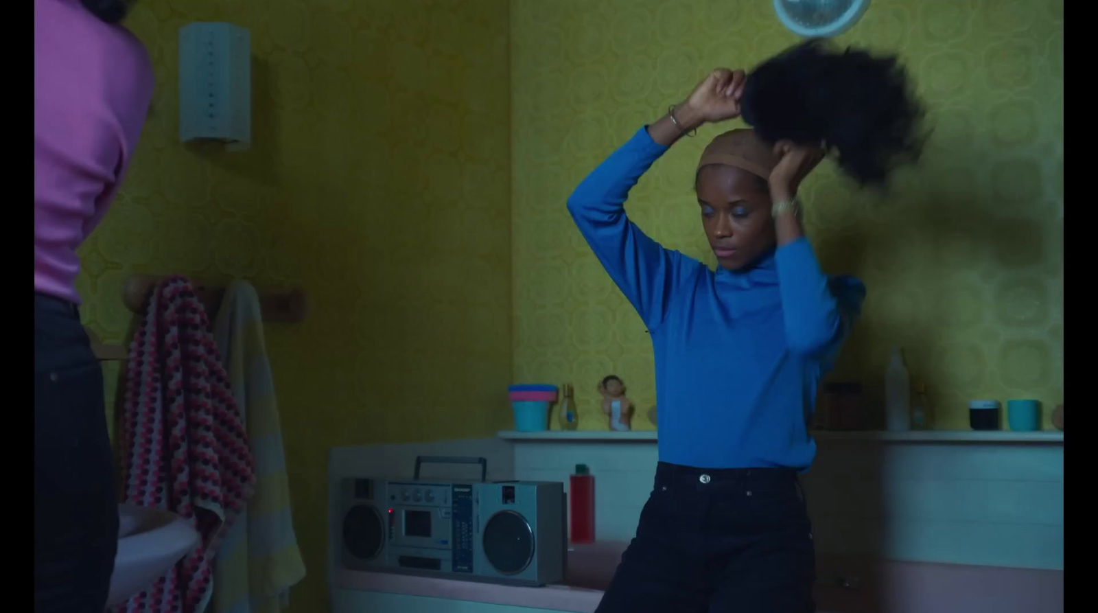 a young girl standing in a bathroom holding a hair dryer on her head