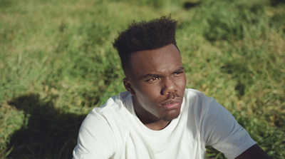 a man sitting in the grass wearing a white shirt