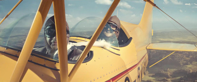 a man sitting inside of a yellow plane flying through the sky