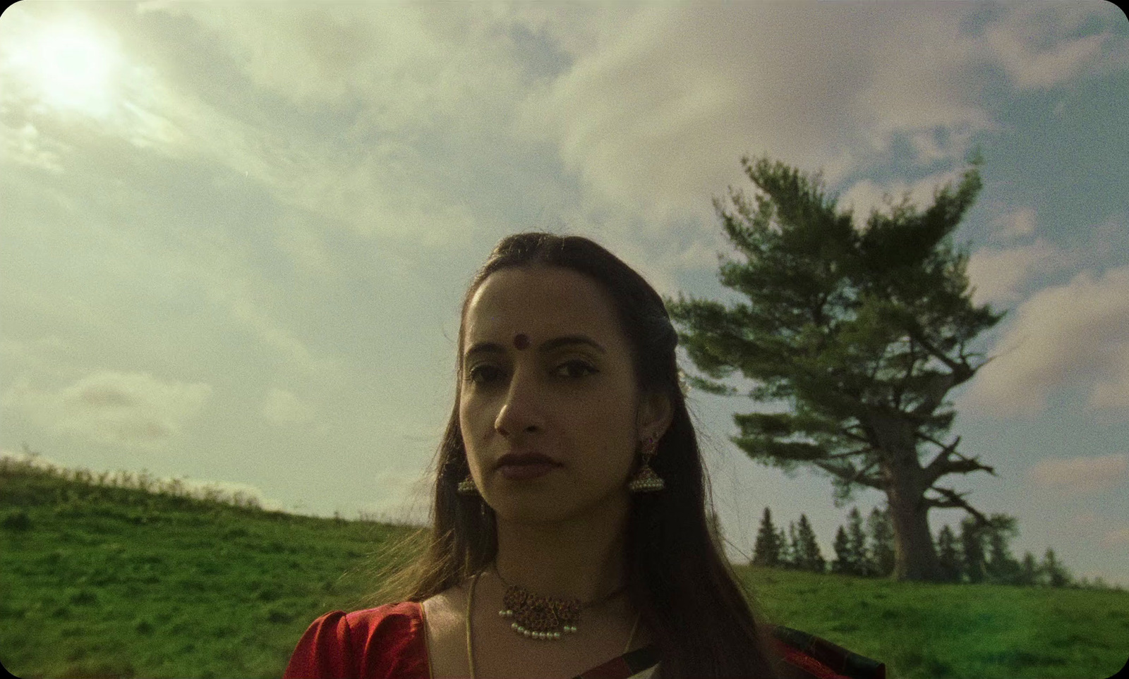 a woman standing in a field with a tree in the background