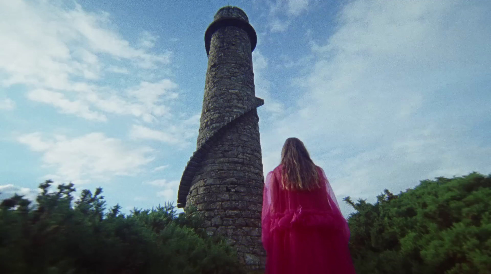 a woman in a red dress standing next to a stone tower