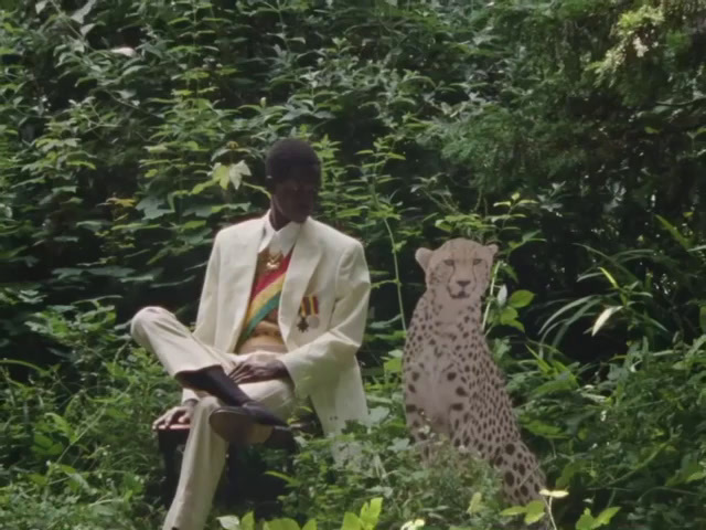 a man in a white suit sitting next to a cheetah