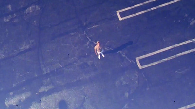 an aerial view of a shirtless man standing in the middle of a parking lot