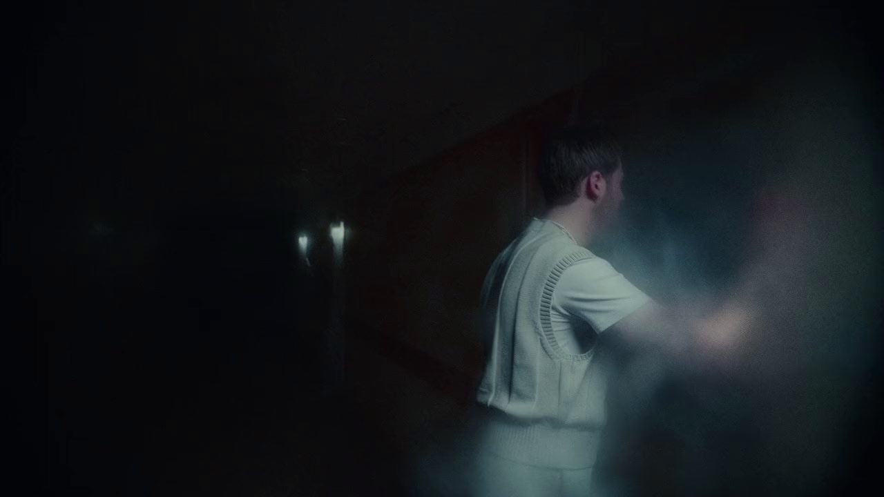 a man in a white shirt standing in a dark room