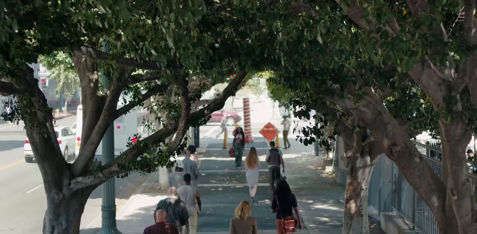 a group of people walking down a sidewalk next to trees