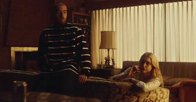 a man standing next to a woman sitting on a couch