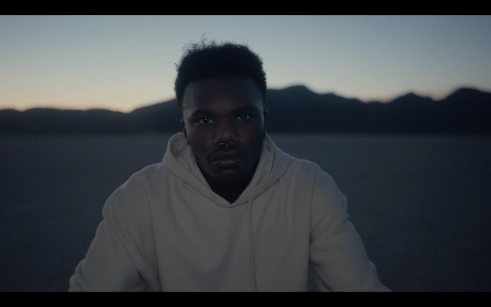 a man in a hoodie sitting in the middle of a desert