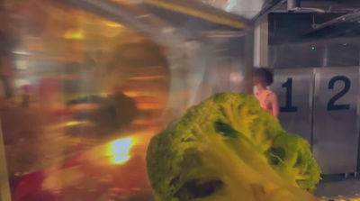 a woman standing in a kitchen next to a large head of lettuce