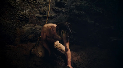 a naked man in a cave with a rope