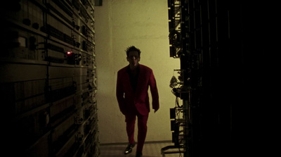 a man in a red suit walking down a dark hallway