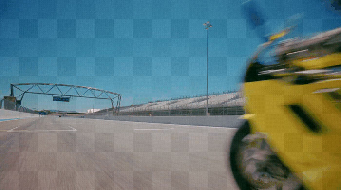 a yellow motorcycle driving down a street next to a bridge