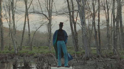 a man in a top hat and blue pants standing in a swamp