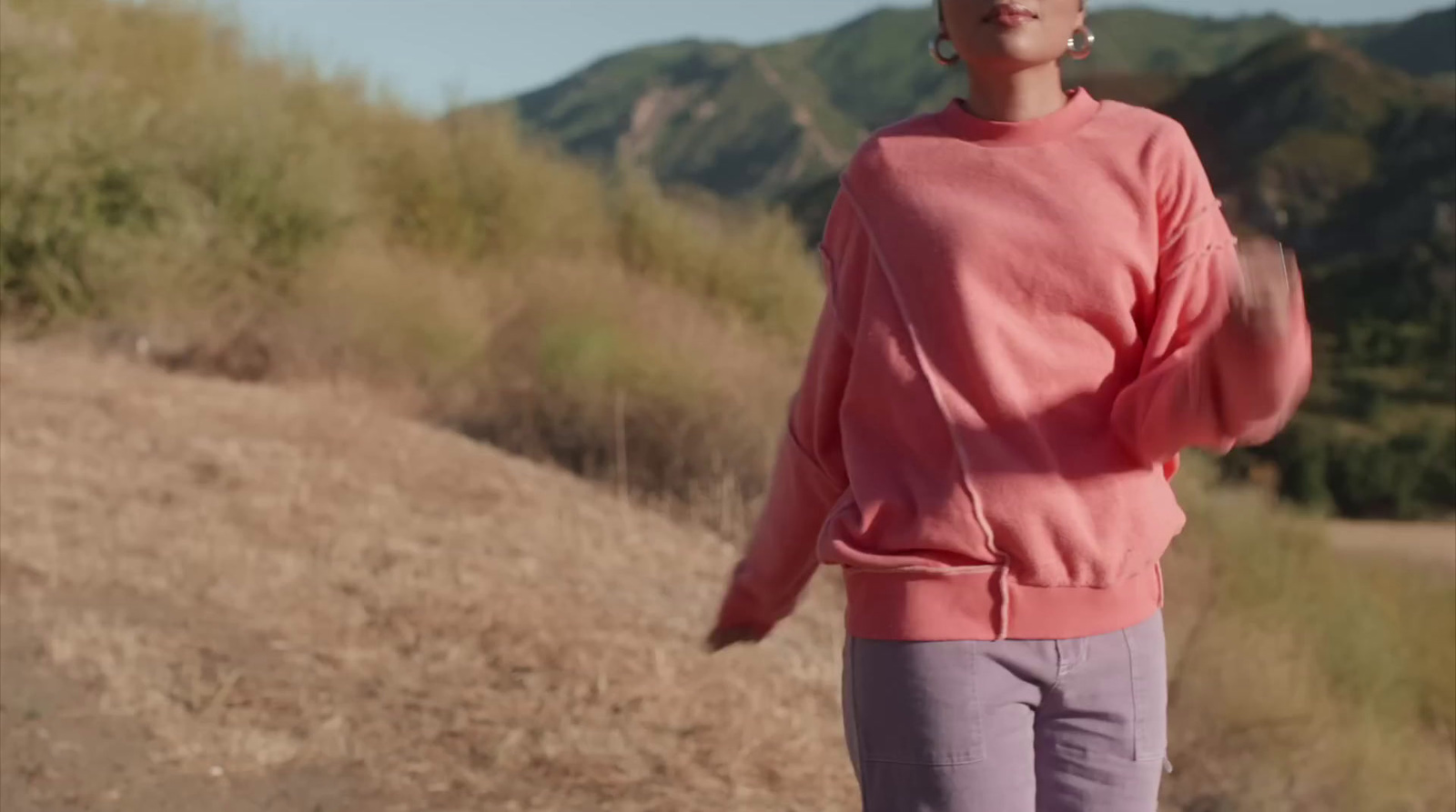 a woman in a pink sweater is standing on a hill