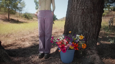 a woman standing next to a tree with a bucket of flowers