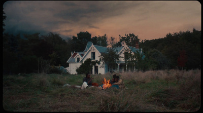 two people sitting around a fire in a field