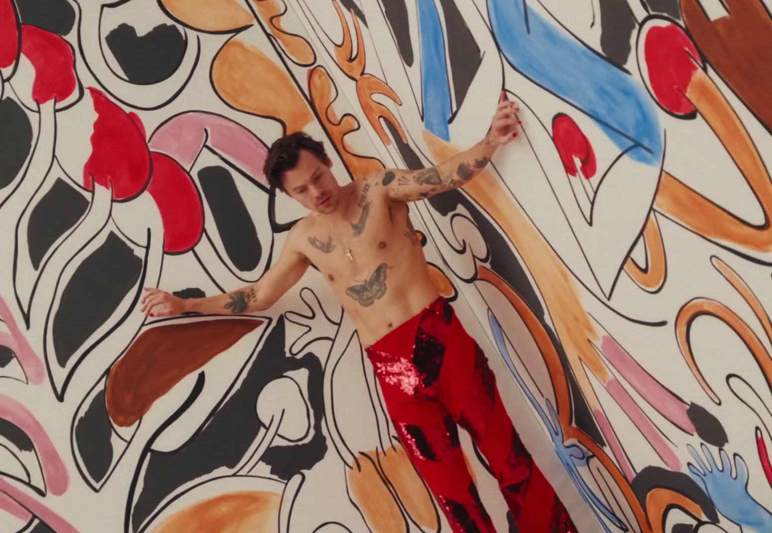 a man with tattoos standing in front of a colorful wall