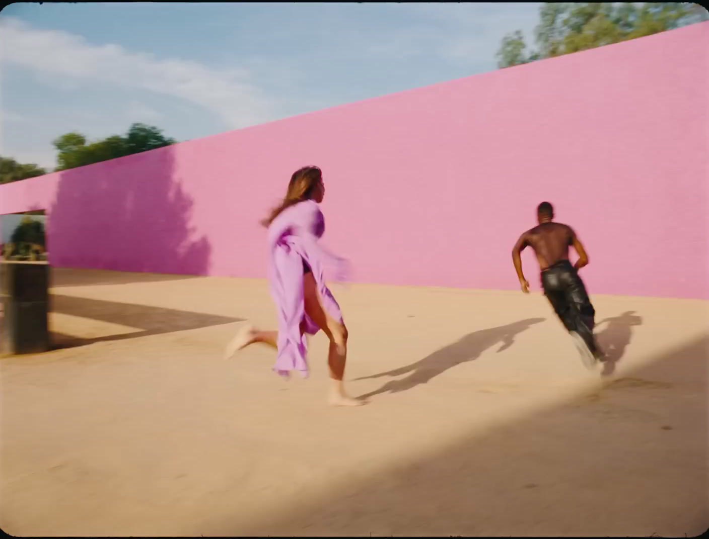 a man and a woman walking in front of a pink wall