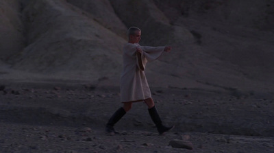 a woman in a white dress and black boots walking in the desert