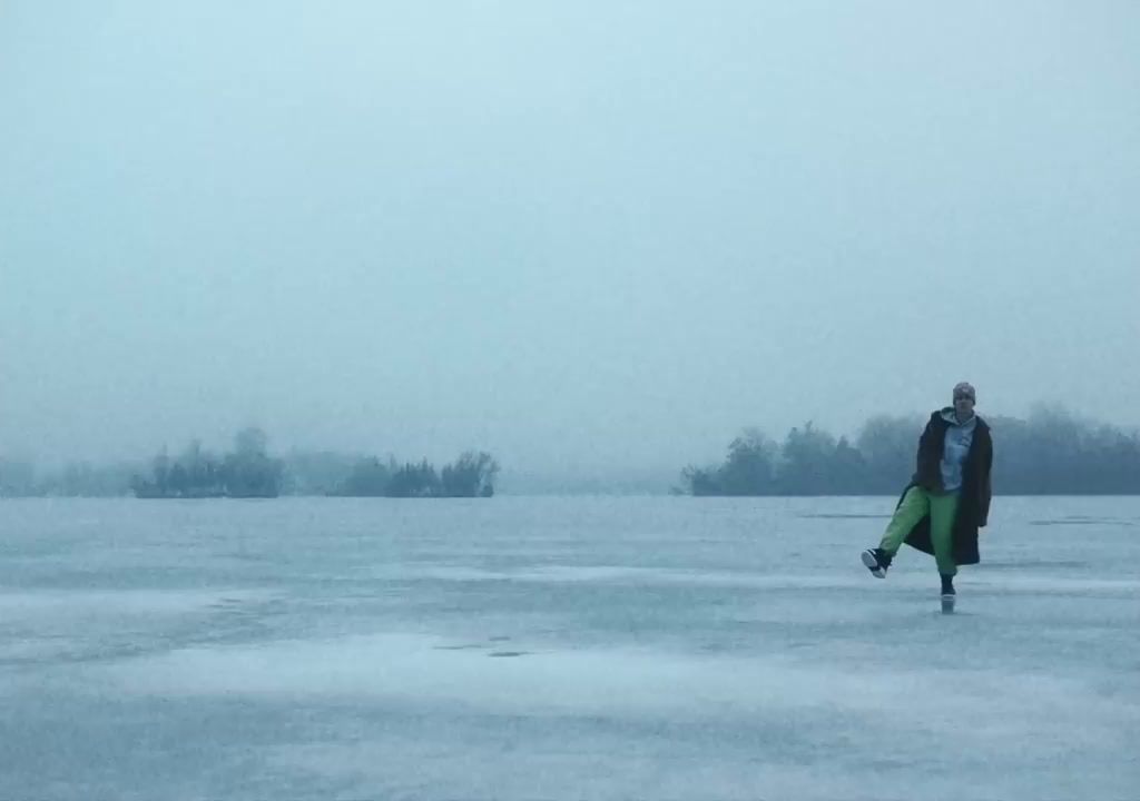 a man walking across a frozen lake holding a surfboard