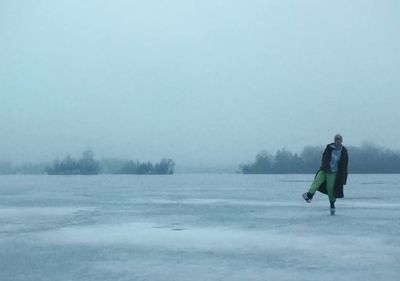 a man walking across a frozen lake holding a surfboard