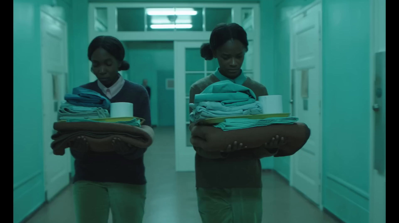 two women carrying blankets in a hallway