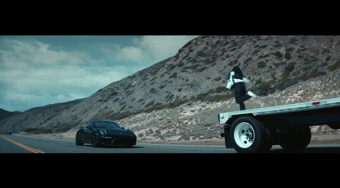 a man standing on the back of a truck next to a black car