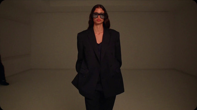 a woman in a black suit and sunglasses walking down a runway