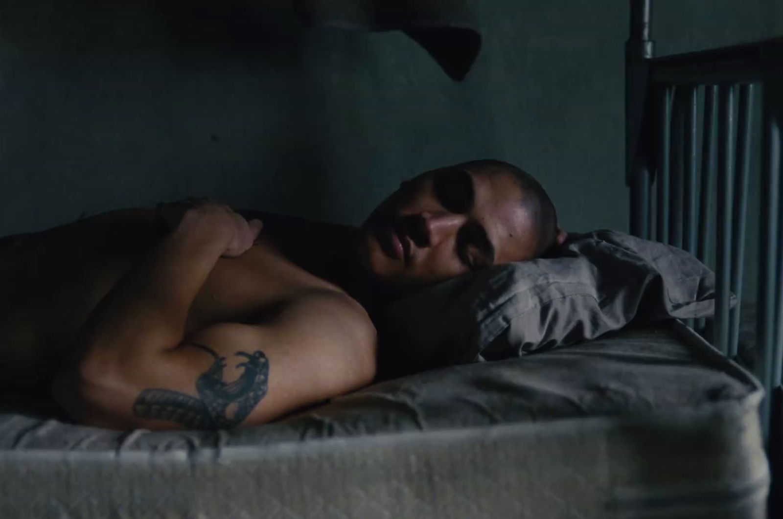 a shirtless man laying on a bed in a dark room