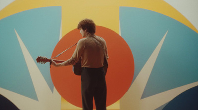 a man standing in front of a colorful wall with a guitar