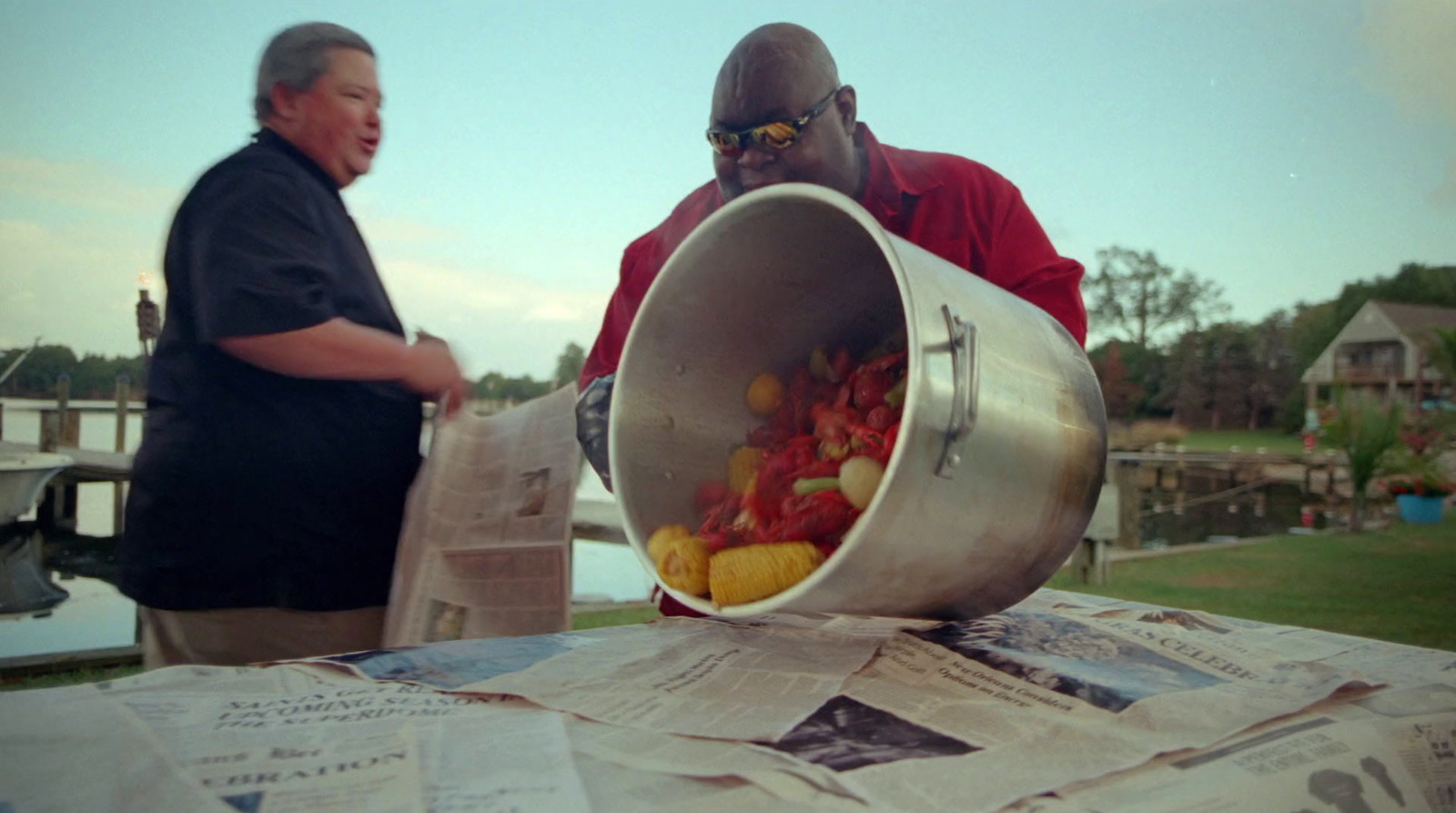 a man standing next to a man holding a metal bucket filled with fruit